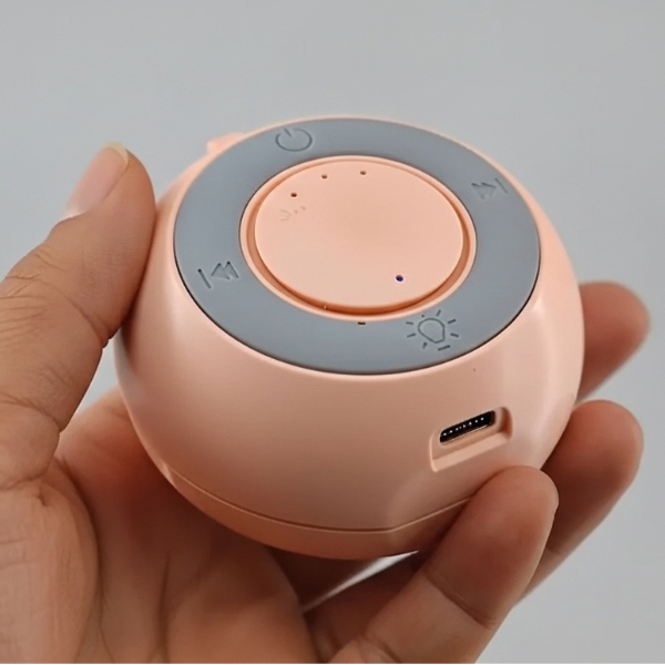 Hand holding a small round electronic device with a peach-colored body and gray top.
